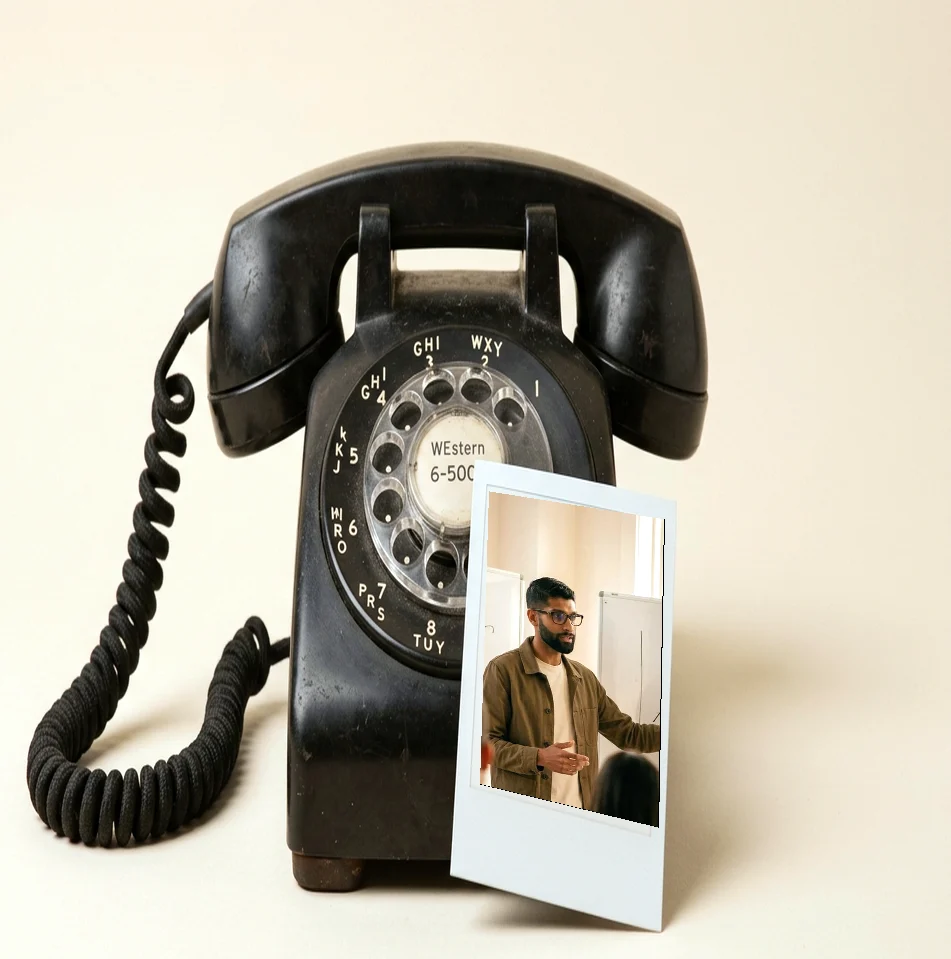 A black rotary desk phone with a photo of Amit at a whiteboard leaning against it